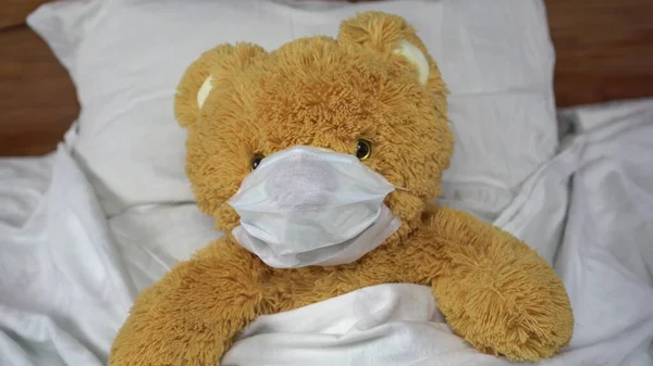 Un oso de peluche yace en la cama con una máscara médica. El oso se enfermó. . — Foto de Stock