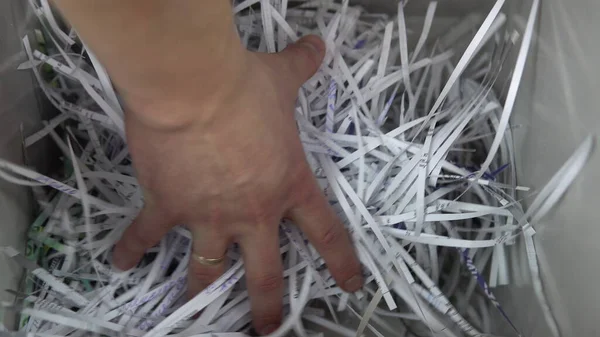 A man picks up trash from a shredder container. Shredder cuts paper and leaves a lot of debris. View on container