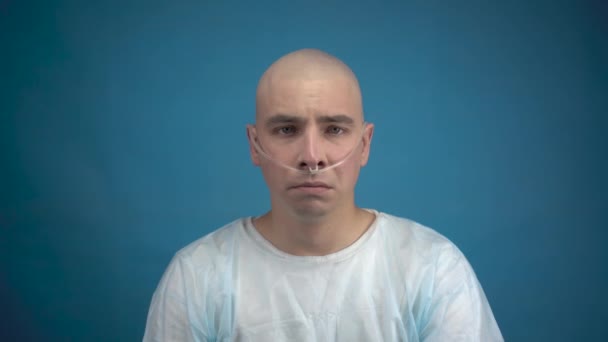 Łysy młody człowiek z onkologią niestety patrzy w obiektyw na niebieskim tle. Utrata włosów w wyniku chemioterapii. — Wideo stockowe