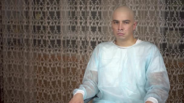 Egy kopasz, rákos fiatalember a kamerába néz és sír. A beteg eltakarja az arcát a kezével, miközben otthon ül egy tolószékben. Kemoterápia miatti hajhullás. — Stock videók