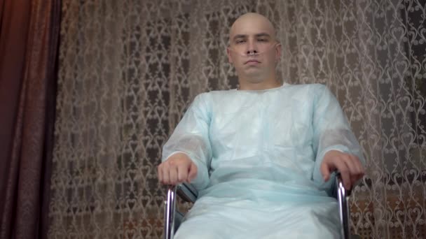 Un jeune homme chauve avec un cancer regarde la caméra et pleure. Le patient se couvre le visage avec ses mains alors qu'il est assis dans un fauteuil roulant à la maison. Perte de cheveux due à la chimiothérapie. — Video