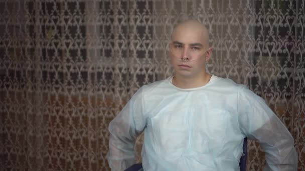 Un giovane calvo con l'oncologia guarda tristemente la telecamera. Un uomo su una sedia a rotelle a casa. Perdita di capelli a causa della chemioterapia. — Video Stock
