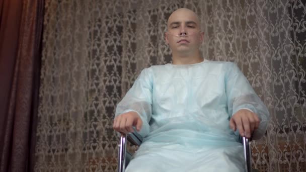 Egy kopasz, rákos fiatalember a kamerába néz és imádkozik. A beteg összecsukta a karját és tolószékben imádkozott otthon. Kemoterápia miatti hajhullás. — Stock videók