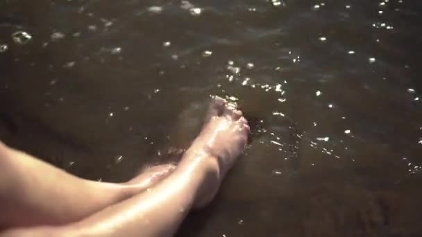 Une jeune femme s'éclabousse les pieds dans une rivière sale. Jambes rapprochées. — Video