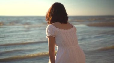 Çekici genç bir kadın sahilde oturur ve denize bakar. Beyaz elbiseli kız sırt üstü oturuyor..