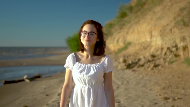 Atrakcyjna młoda kobieta spaceruje wzdłuż plaży morskiej. Dziewczyna w białej sukience spaceruje po plaży z bliska. Zwolniony ruch. — Wideo stockowe