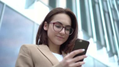Bir iş merkezinin arka planında telefonu olan genç bir kadın. Paltolu kız akıllı telefondan mesaj atıyor..