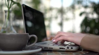 Genç iş kadını bir kafede oturuyor ve yakın plan dizüstü bilgisayarda çalışıyor. Yaz verandasında kahve içen kız..