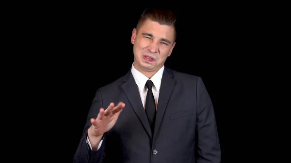 Genç işadamı yaklaşık olarak bir el hareketi gösteriyor. Siyah arka planda siyah takım elbiseli adam.