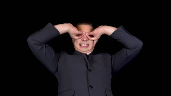 Young businessman makes a superhero mask from hands. Man in a black suit on a black background — Stock Photo, Image