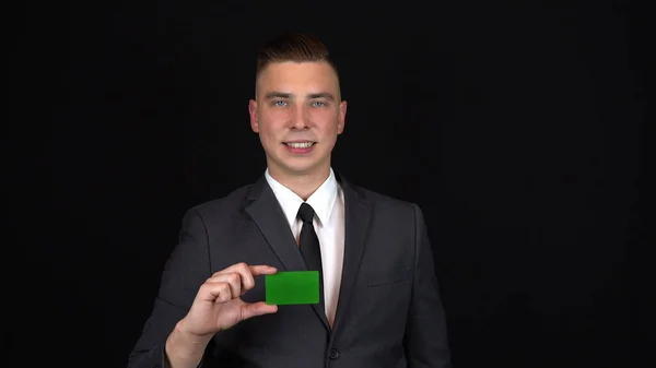 Un jeune homme d'affaires en costume tient une carte bancaire en main. Fond noir isolé. Carte verte Chromakey. 4k — Photo