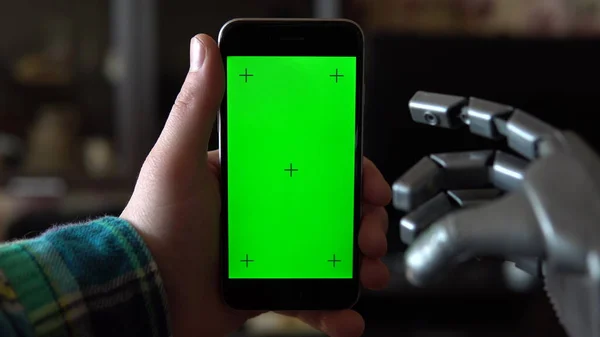 Cyborg használja a telefont. Gray mechanikus kéz húzza le okostelefon zöld képernyőn. Kroma kulcs. — Stock Fotó