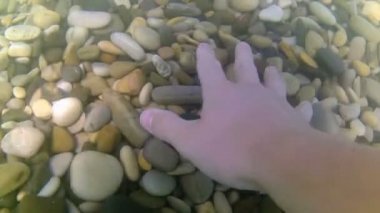 Genç bir adam taşları için denize dalıyor. Yakın plan el, aşağıdan taş topluyor..