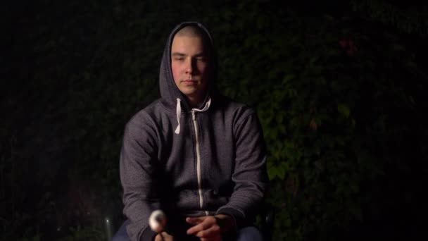 젊은 남자가 담배를 피우고 불위에서 마시멜로를 먹습니다. 밤의 캠프파이어. — 비디오