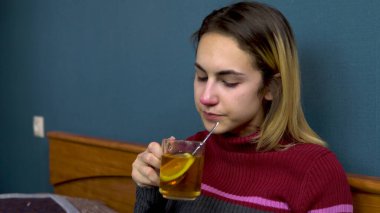 Genç bir kadın limonlu çay içer. Kız hasta yatağında yatıyor. Etrafa saçılmış kağıt eşarplar
