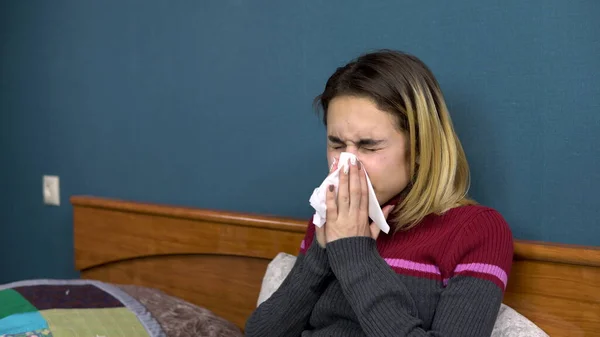 A young woman sneezes and blows her nose in a napkin. The girl is sick lying on the bed. Closeup — Stock Photo, Image