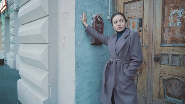 Девушка в лиловом пальто стоит на улице у двери старого здания — стоковое фото