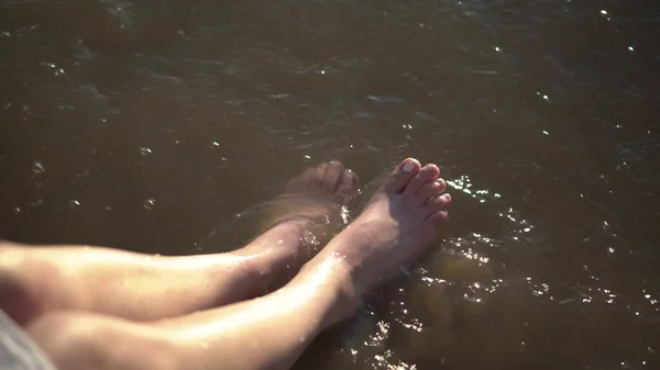 Junge Frau planscht ihre Füße in einem schmutzigen Fluss. Beine aus nächster Nähe. — Stockfoto