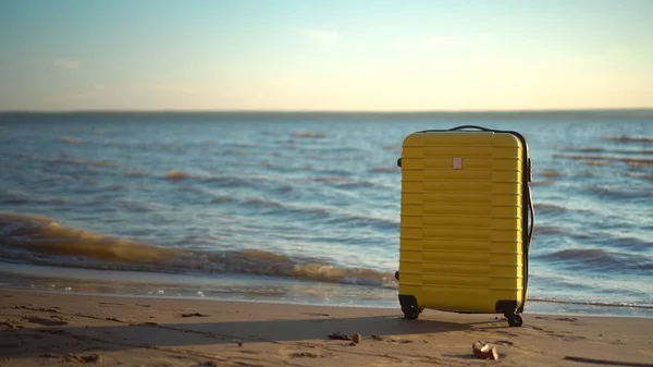 A yellow suitcase stands on the beach against the background of the sea. Travel suitcase. — Stock Photo, Image