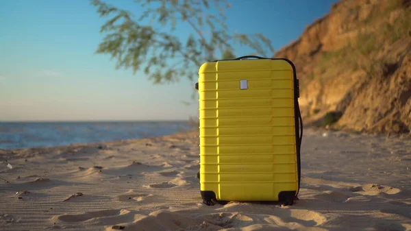 A yellow suitcase stands on the beach against the background of the sea. Travel suitcase. — Stock Photo, Image