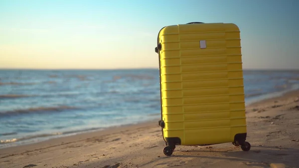 A yellow suitcase stands on the beach against the background of the sea. Travel suitcase. — Stock Photo, Image