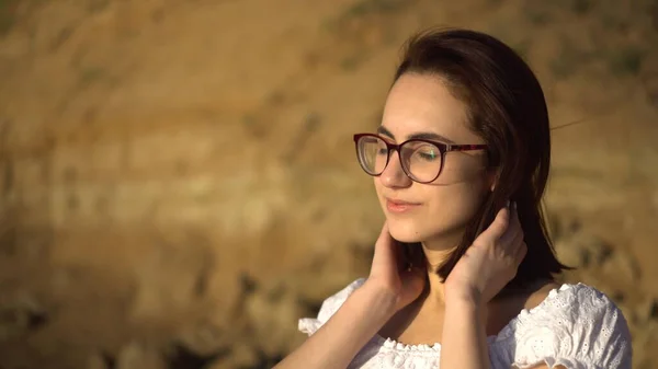 Kil bir kayanın arka planında çekici genç bir kadın. Gözlüklü bir kız saçını düzleştiriyor.. — Stok fotoğraf