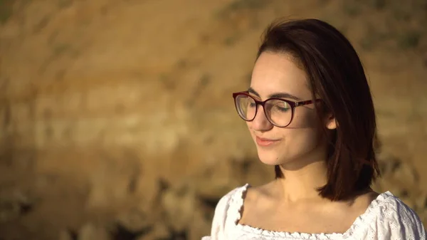 Jolie jeune femme sur le fond d'une roche d'argile. Une fille avec des lunettes redresse ses cheveux gros plan. — Photo