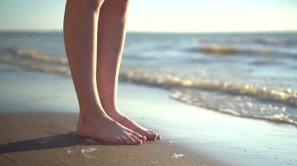 Een jonge vrouw staat blootsvoets op de zandkust. Benen dicht.. — Stockfoto