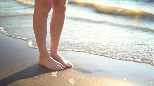 Une jeune femme se tient pieds nus sur le rivage sablonneux. Jambes rapprochées. — Photo