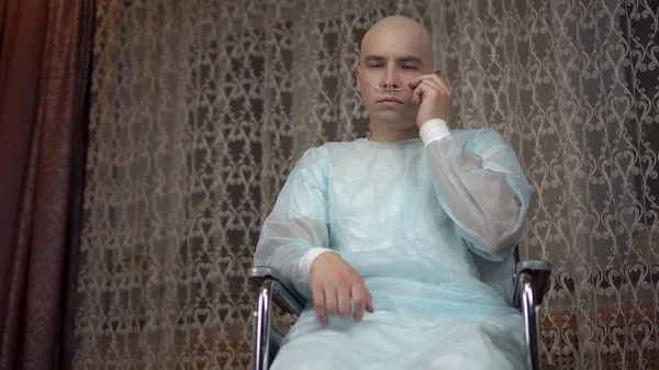 Egy kopasz fiatalember az onkológiával szomorúan néz a kamerába. A beteg állítsa be a légzőkészüléket, miközben otthon ül egy tolószékben. Kemoterápia miatti hajhullás. — Stock Fotó