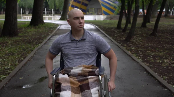 一个得了肿瘤病的年轻人坐着轮椅穿过公园。这个男人因为化疗而秃头. — 图库照片