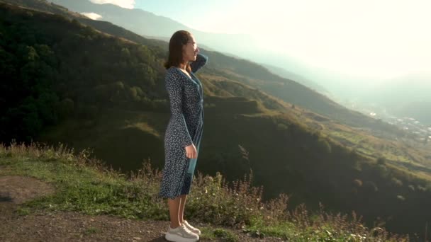 Mladá žena stojí v šatech a dívá se na hory. — Stock video