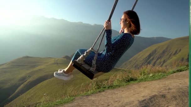 Giovane donna va a fare un giro su un'altalena su uno sfondo di montagne. Rallentatore. — Video Stock