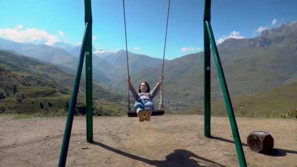 Giovane donna va a fare un giro su un'altalena su uno sfondo di montagne caucasiche. — Video Stock