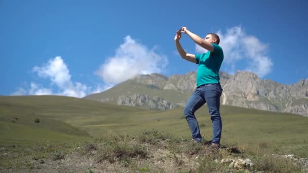 Mladý muž stojí v horách a fotí po telefonu. Muž cestuje po Kavkazských horách. — Stock video