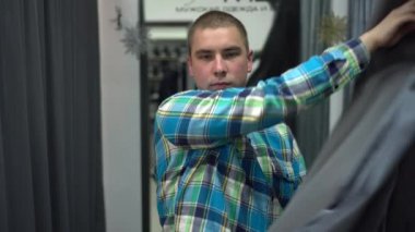 Genç bir adam soyunma odasındaki perdeyi açar. Giysi mağazası.