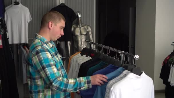 A young man chooses clothes in a store and rejoices at the price of a shirt. Clothing store. — Stock Video