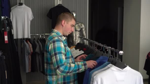 Молодой человек выбирает рубашку в магазине и удивляется дорогостоящей цене рубашки. Магазин одежды. — стоковое видео