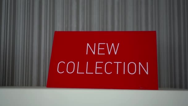 Een rood bord met de woorden "nieuwe collectie" staat in de winkel. Kleding winkel. — Stockvideo