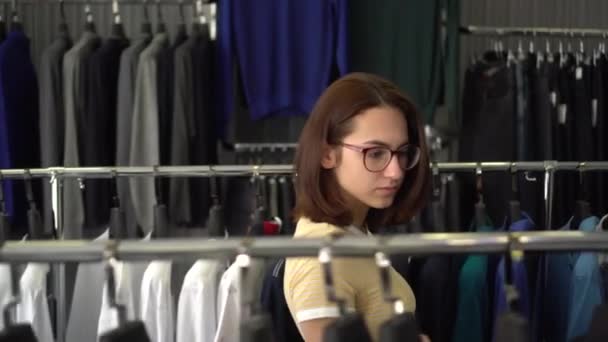 Jonge vrouw kiest kleren in de winkel. Kleding winkel. — Stockvideo