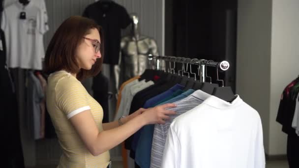 Uma jovem estava escolhendo uma camisa em uma loja. Loja de roupas. — Vídeo de Stock