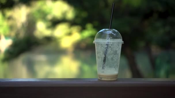 Coupe en plastique debout sur la rampe du pont sur la toile de fond du lac. Il reste du café dans le verre.. — Video