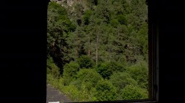Terk edilmiş bir binanın penceresinden yeşil dağların manzarası. Kamera pencereye doğru hareket eder.