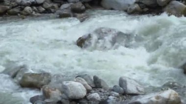 Hızla akan bir dağ nehri manzarası. Kamera suyun hareketini izler..