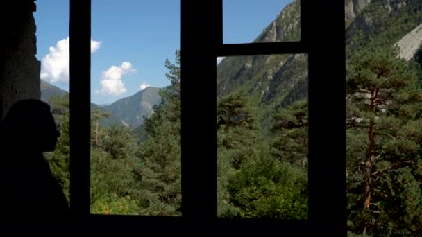 Pohled na zelené hory z okna opuštěné budovy. K oknu přistoupí mladá žena.. — Stock video
