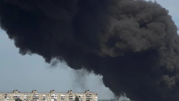 Black smoke rises above the buildings. A big chemical fire at a factory building. Thick black smoke covers the sky.