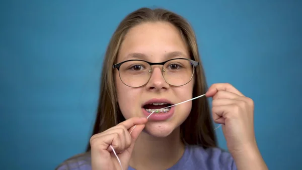 Diş ipiyle dişlerini fırçalayan diş teli takan kız. Dişlerinde renkli diş teli olan bir kız dişlerini temiz tutar..