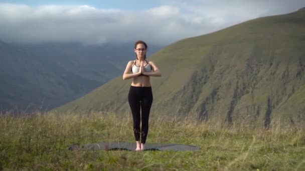 Eine junge Frau im Trainingsanzug praktiziert Yoga und posiert in den Bergen. Die Kamera bewegt sich und erzeugt einen Parallaxe-Effekt. — Stockvideo