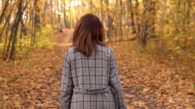 Sonbahar ormanında gözlüklü ve ceketli genç bir kadın yürüyor. Sarı yapraklar var. Yavaş çekim