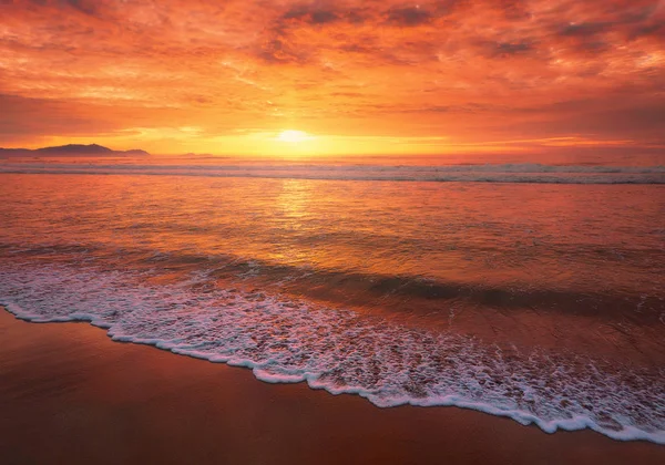 Belo pôr do sol vermelho na praia com uma onda na costa — Fotografia de Stock